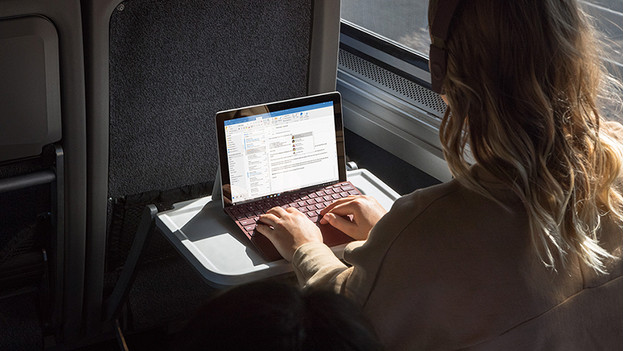 Vrouw werkt op Surface Go laptop in trein. 