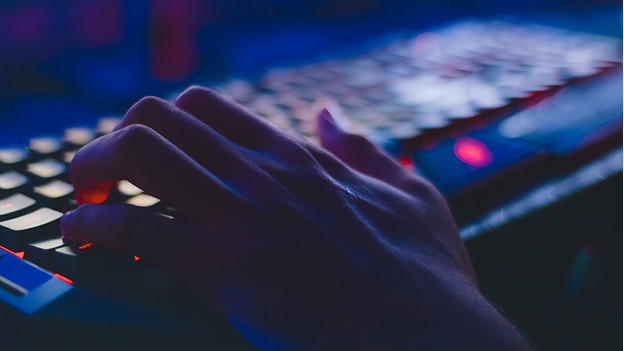 Hand rests on gaming keyboard that lights up in the dark.