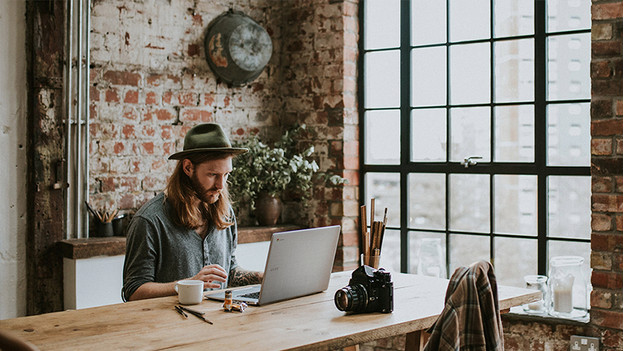 Hipster met lang haar en hoed werkt achter Acer Chromebook. Camera ligt op tafel. 