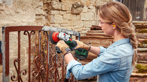 Person removes rust from the gate with an angle grinder by Bosch