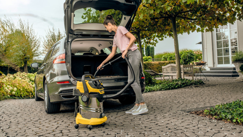 Vrouw gebruikt Karcher bouwstofzuiger om auto schoon te maken.