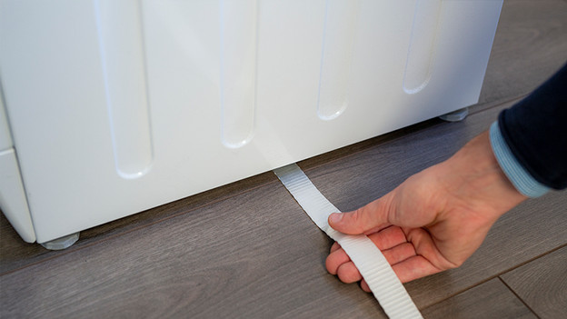 Trek de riem onder de wasmachine door en houd de riem in het midden. 