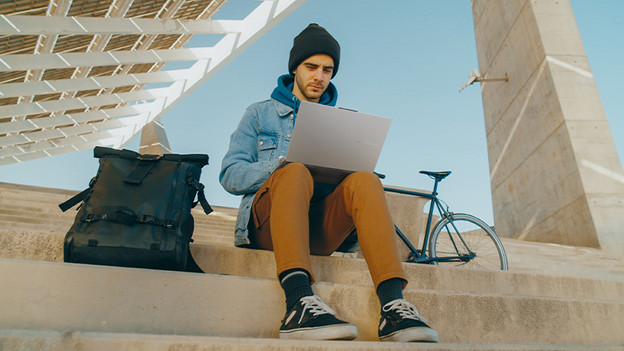 Meisje typt op laptop. Een telefoon ligt op de tafel. 