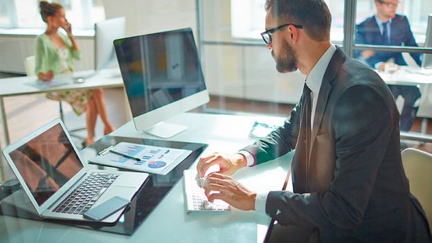 Man at the office works behind his desk with a laptop and keyboard.
