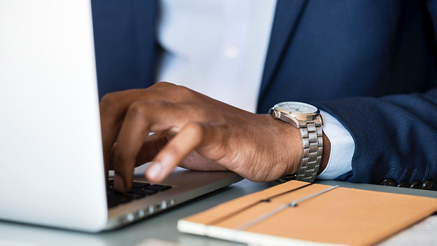 Businessman works on laptop. There's a notebook on the table next to him.