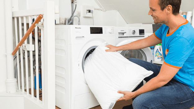 Man stop hoofdkussen in wasmachine.